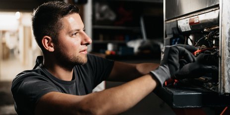 In einer Werkstatt repariert ein Mann ein Gerät, seine Gesichtszüge zeigen Entschlossenheit und Konzentration auf die Aufgabe.