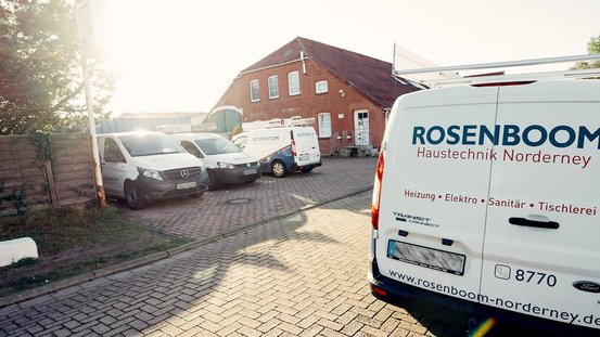 Eine Reihe von Lieferwagen der Firma Rosenboom steht auf einem gepflasterten Parkplatz vor einem roten Backsteingebäude.