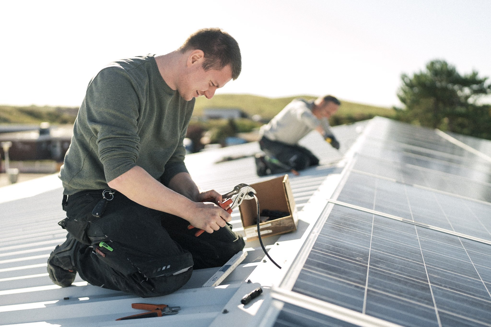 Ein Handwerker arbeitet konzentriert an der Installation von Solarpanelen auf einem Dach, während ein Kollege im Hintergrund hilft.