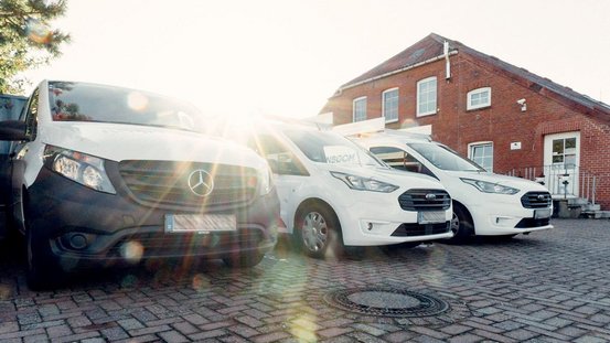 Drei Lieferwagen stehen auf einem gepflasterten Parkplatz, während die Sonne im Hintergrund strahlt und eine warme Atmosphäre schafft.
