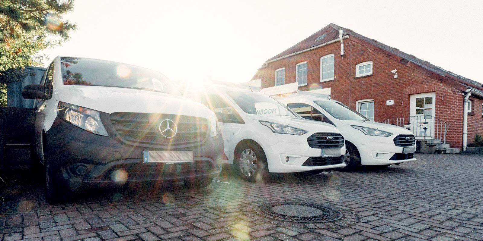 Drei Lieferwagen stehen auf einem gepflasterten Parkplatz, während die Sonne im Hintergrund strahlt und eine warme Atmosphäre schafft.