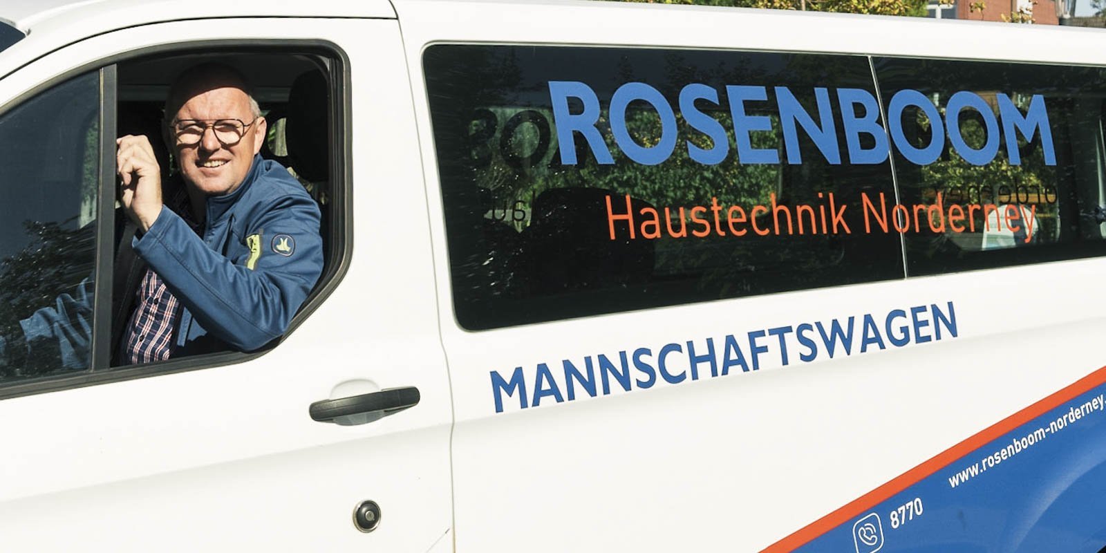 Ein lächelnder Mann mit Brille sitzt am Steuer eines weißen Fahrzeugs mit dem Schriftzug 'Rosenboom'.