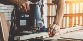Ein Handwerker benutzt eine Stichsäge, um präzise Schnitte in ein Holzstück zu machen, während Sonnenlicht durch das Fenster strömt.