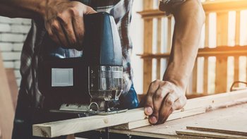 Ein Handwerker benutzt eine Stichsäge, um präzise Schnitte in ein Holzstück zu machen, während Sonnenlicht durch das Fenster strömt.