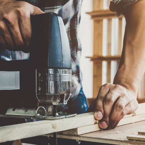 Ein Handwerker benutzt eine Stichsäge, um präzise Schnitte in ein Holzstück zu machen, während Sonnenlicht durch das Fenster strömt.