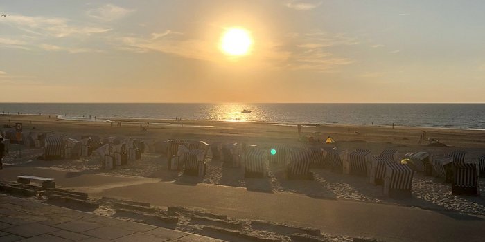 Die goldene Sonne strahlt über den Horizont, während Menschen am Strand spazieren und die ruhige Atmosphäre genießen.