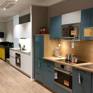 Moderne Küche mit blauen und weißen Schränken, Holzregalen und Edelstahlgeräten, die ein einladendes Ambiente schaffen.